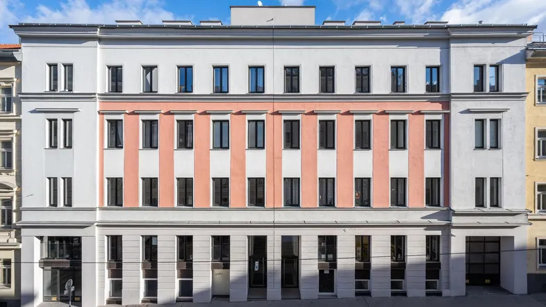 Moderne Fassade eines Mehrfamilienhauses mit weißer und rosafarbener Gestaltung unter blauem Himmel.