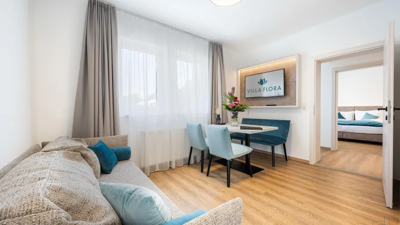Helles Wohn- und Esszimmer mit modernem Mobiliar und Zugang zu einem Schlafzimmer.