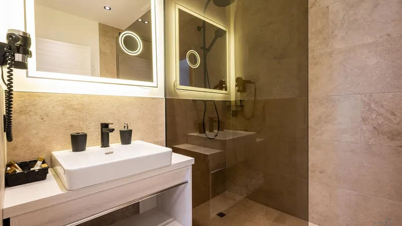 Modernes Badezimmer mit begehbarer Dusche, Einzelwaschbecken und beleuchtetem Spiegel.