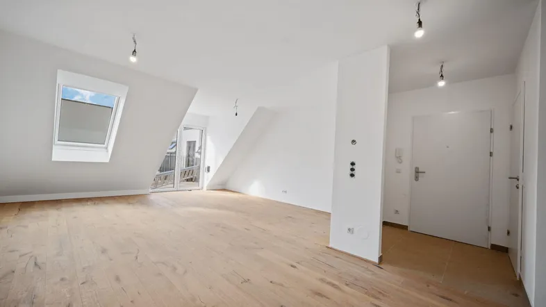 Helles Zimmer mit Holzboden, Dachschrägen und Zugang zu einem kleinen Balkon.