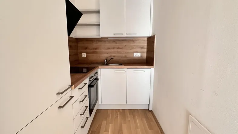 Moderne Einbauküche mit weißen Schränken, Holzakzenten und Parkettboden.