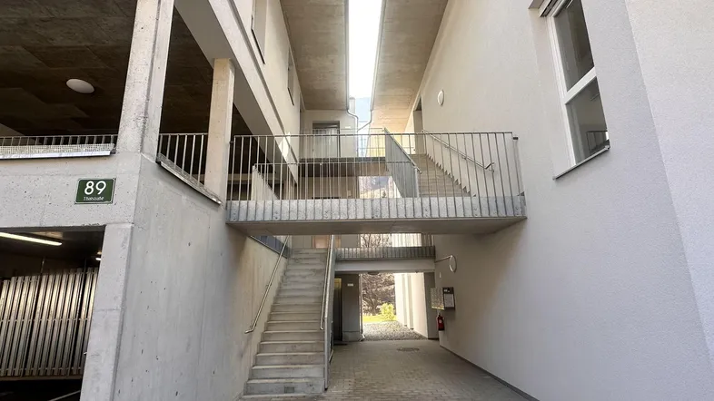 Eingangsbereich eines modernen Wohngebäudes mit Treppen, Gehwegen und Zugang zur Tiefgarage.