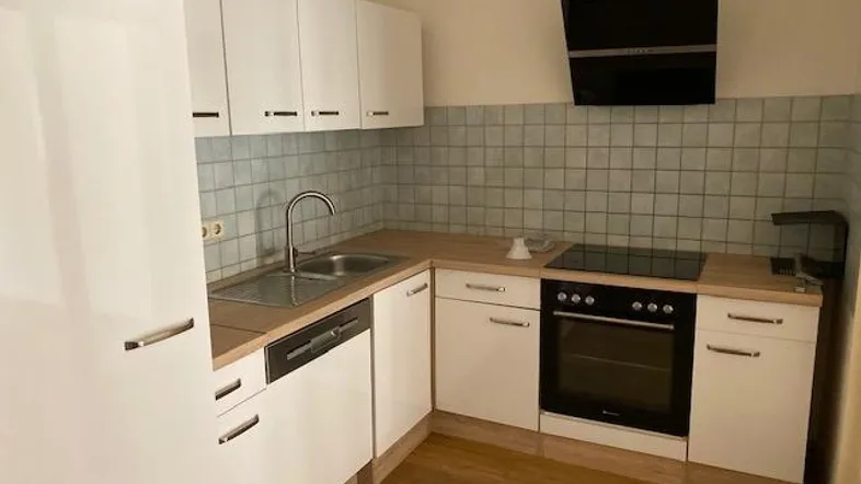 Moderne Einbauküche mit weißen Schränken, Holzoptik-Arbeitsplatte und integrierten Geräten.