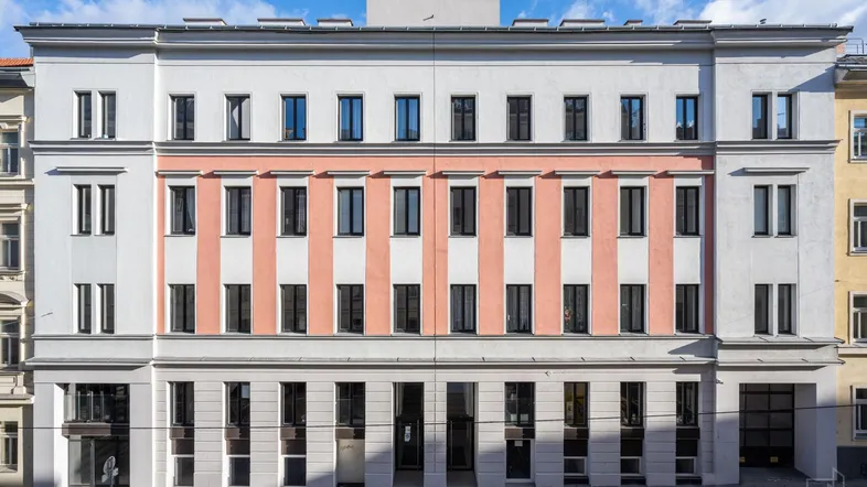Die moderne Fassade des Gebäudes mit hellen und rosafarbenen Streifen sowie vielen Fenstern.