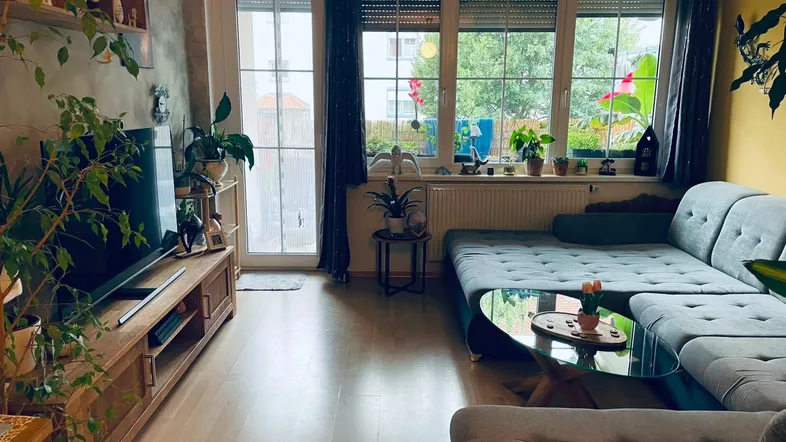 Helles Wohnzimmer mit großem Sofa, Holzboden und Zugang zum Balkon.