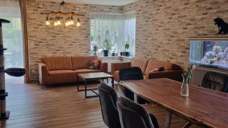 Geräumiger Wohn-Essbereich mit bequemen Sofas, großem Esstisch und dekorativer Ziegelwand.