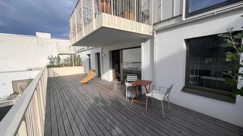 Geräumige Holzterrasse mit Sitzgelegenheiten und einem darüberliegenden Balkon, ideal für Entspannung im Freien.