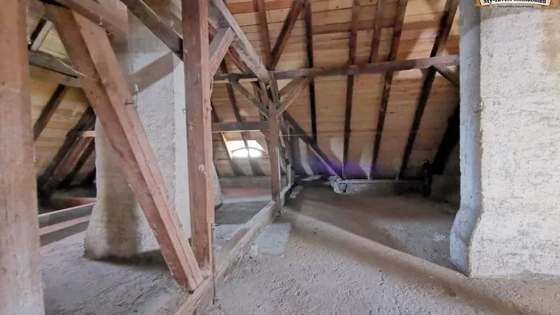 Unausgebauter Dachboden mit sichtbaren Holzbalken, Dachschrägenfenstern und rohem Betonboden, bereit für den Ausbau.