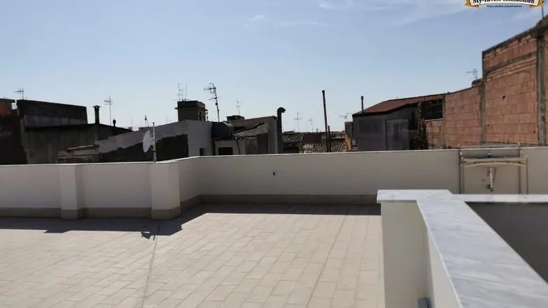 Geräumige Dachterrasse mit hellen Fliesen und weitem Blick über die umliegenden Dächer der Stadt.