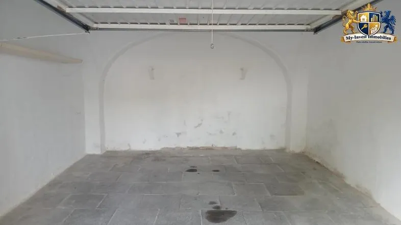 Innenansicht einer Garage mit gewölbter Wand, Steinboden und sichtbarer Deckenkonstruktion.