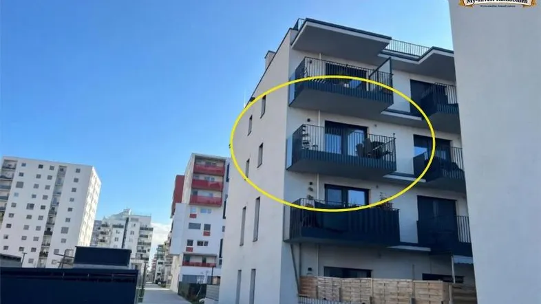Modernes Mehrfamilienhaus mit mehreren Balkonen und klarem Himmel, umgeben von weiteren Gebäuden.