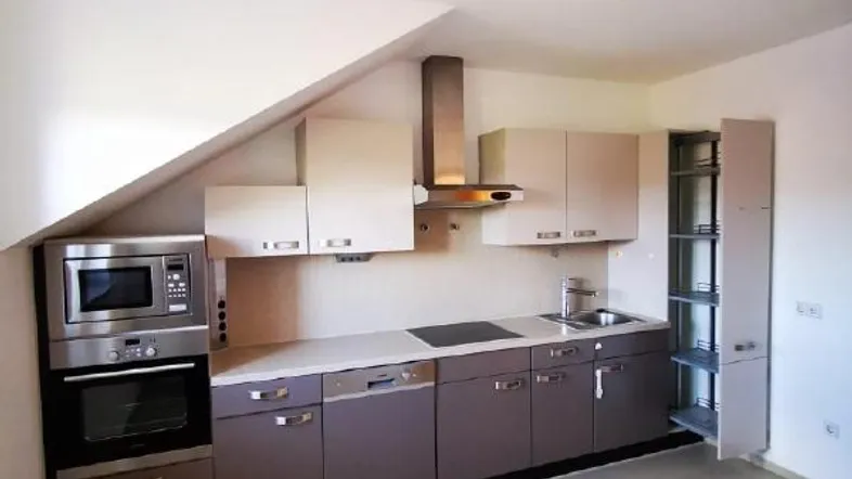 Moderne Einbauküche mit Dachschräge, ausgestattet mit Geräten und ausreichend Stauraum.