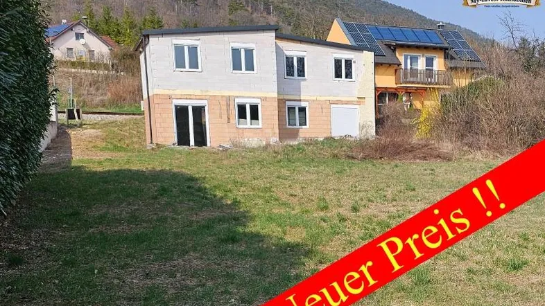 Haus im Rohbauzustand mit Baustelle und Bergkulisse, bereit für den Innenausbau.