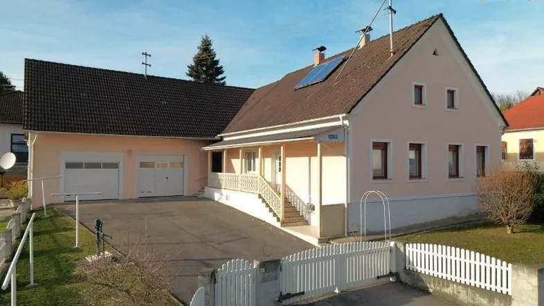 Freistehendes Einfamilienhaus mit beiger Fassade, Satteldach, Doppelgarage und gepflegtem Vorgarten.