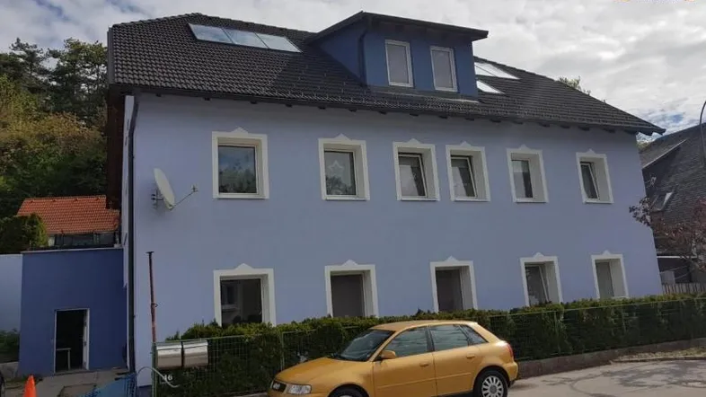 Blau gestrichenes Wohnhaus mit dunklem Dach und mehreren Fenstern an einem sonnigen Tag.