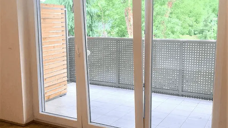 Heller Raum mit Holzboden und großer Schiebetür, die auf einen Balkon führt.