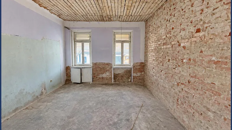 Unrenovierter Raum mit freigelegten Ziegelwänden und Holzbalkendecke, bereit für die Sanierung.