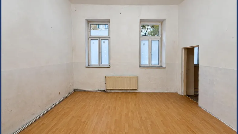Geräumiges, unmöbliertes Zimmer mit Laminatboden, hohen Decken und zwei Fenstern.