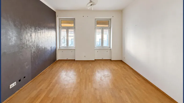 Helles Zimmer mit Parkettboden und einer dunkelgrauen Akzentwand, bereit zur individuellen Gestaltung.