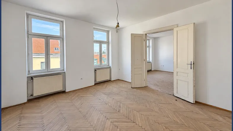 Helles Zimmer mit Fischgrätparkettboden, weißen Wänden und Blick auf die umliegenden Gebäude.