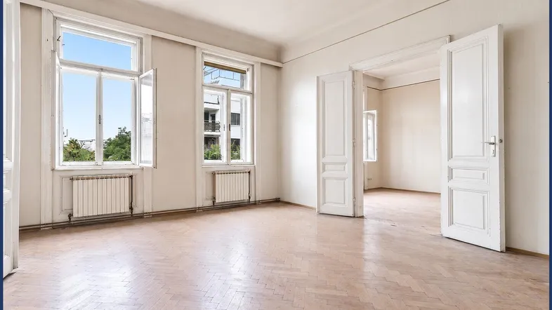 Helles, geräumiges Zimmer mit Fischgrätparkett und hohen Fenstern, bereit zur Renovierung.