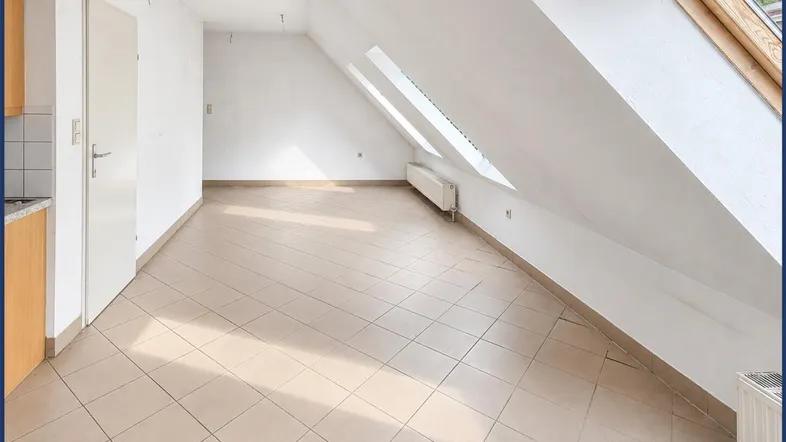 Helles Dachgeschoss-Wohnzimmer mit Fliesenboden, Dachfenstern und integrierter Küchenzeile.