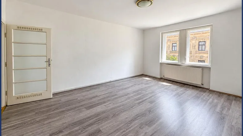 Helles, leeres Zimmer mit Laminatboden und Blick auf die gegenüberliegende Fassade.