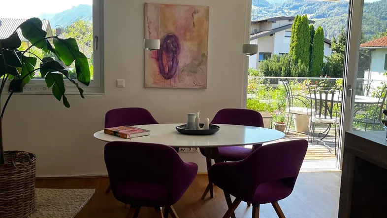 Heller Essbereich mit Holzboden, runden Tisch, lila Stühlen und Zugang zur Terrasse mit Bergblick.