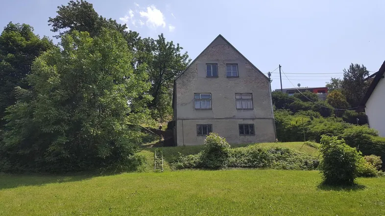 Altes Haus mit Satteldach und großem Garten auf einem Hanggrundstück.