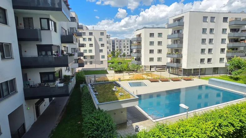 Moderne Wohngebäude mit Gemeinschaftspool und Grünflächen unter blauem Himmel.