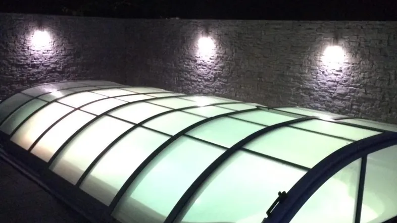 Überdachter Poolbereich bei Nacht mit stimmungsvoller Beleuchtung und Steinmauer im Hintergrund.