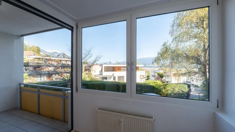 Heller Innenraum mit Holzboden, Heizkörper und Zugang zu einem Balkon mit Bergblick.