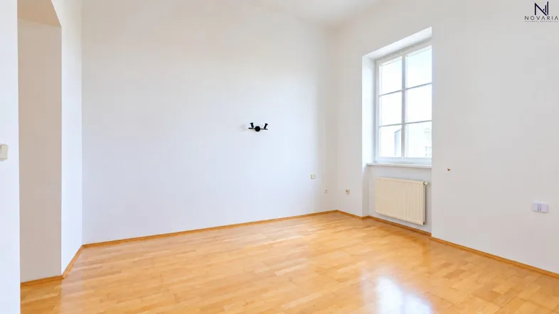 Helles Zimmer mit Parkettboden und großem Fenster, ideal als Wohn- oder Schlafbereich.