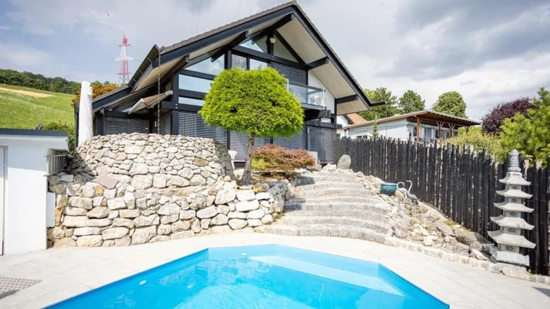 Modernes Haus mit markanter Architektur, umgeben von Natur und einem erfrischenden Poolbereich.