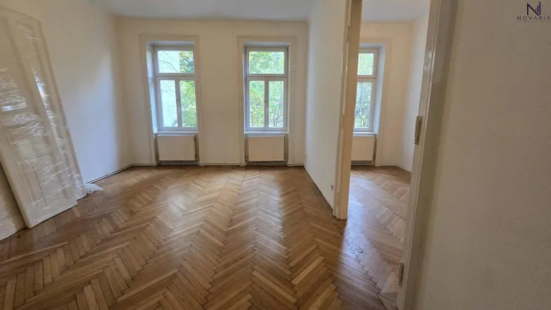 Helles Zimmer mit klassischem Fischgrätparkett, weißen Wänden und mehreren Fenstern, bereit zur Gestaltung.