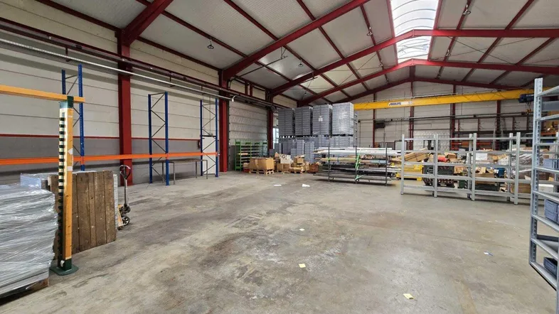 Große Lagerhalle mit hohen Decken, sichtbaren Stahlträgern und Betonboden für industrielle Nutzung.