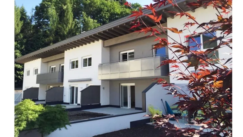 Moderne Reihenhäuser mit Balkonen und Terrassen in grüner Umgebung und Holzbalken.