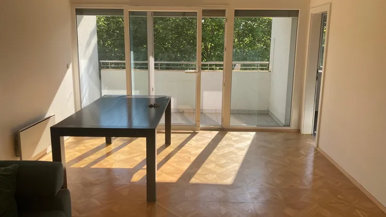 Helles Wohnzimmer mit Parkettboden, großem Esstisch und Zugang zum Balkon.