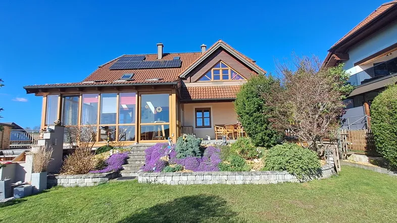 Charmantes Einfamilienhaus mit Wintergarten, Solaranlage und gepflegtem Vorgarten unter blauem Himmel.