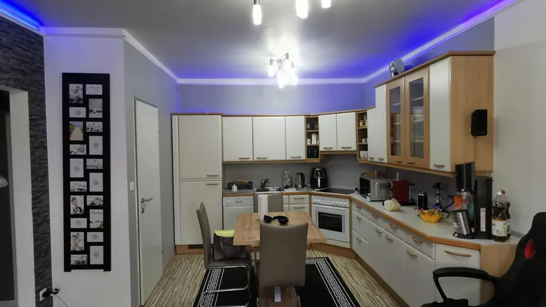 Moderne Küche mit Essbereich, blauer LED-Beleuchtung und Laminatboden, offen zum Wohnbereich.