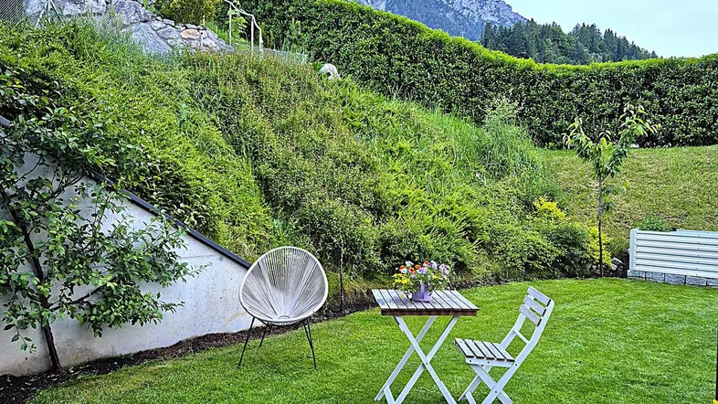 Grüner Garten mit Sitzgelegenheit und beeindruckendem Bergblick unter bewölktem Himmel.