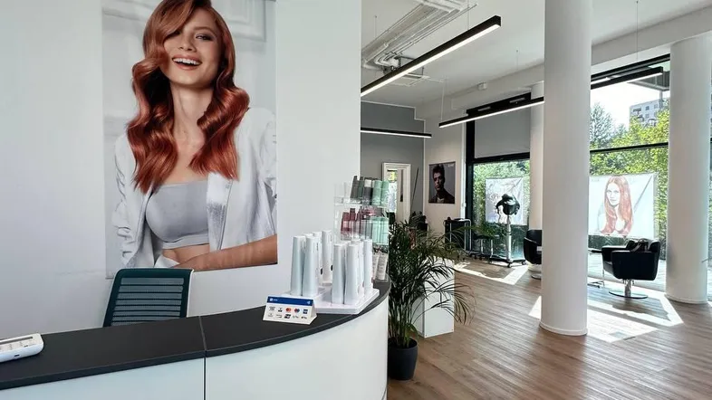 Moderner Empfangsbereich eines Friseursalons mit weißer Theke, Holzboden und großen Fenstern für viel Tageslicht.