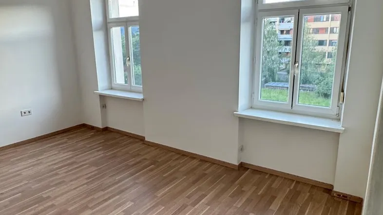 Helles Zimmer mit Holzdielenboden und zwei Fenstern, bereit zur individuellen Gestaltung.