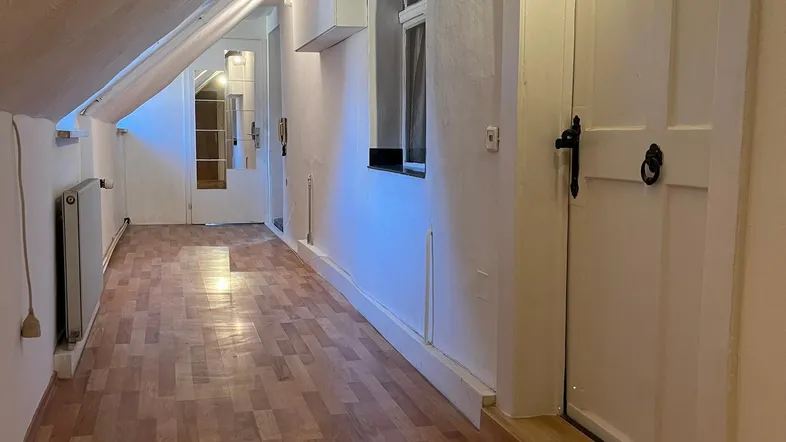 Langer Flur im Dachgeschoss mit schrägen Wänden, Holzfußboden und Fenstern, die für Helligkeit sorgen.