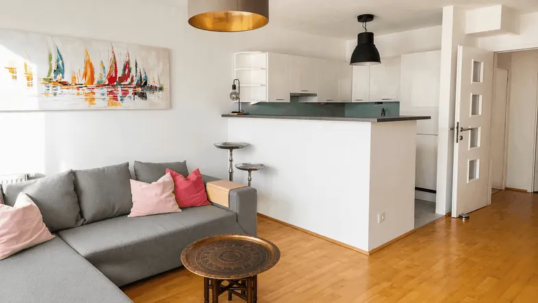 Helles Wohnzimmer mit offener Küche, bequemer Couch und modernem Segelbild an der Wand.