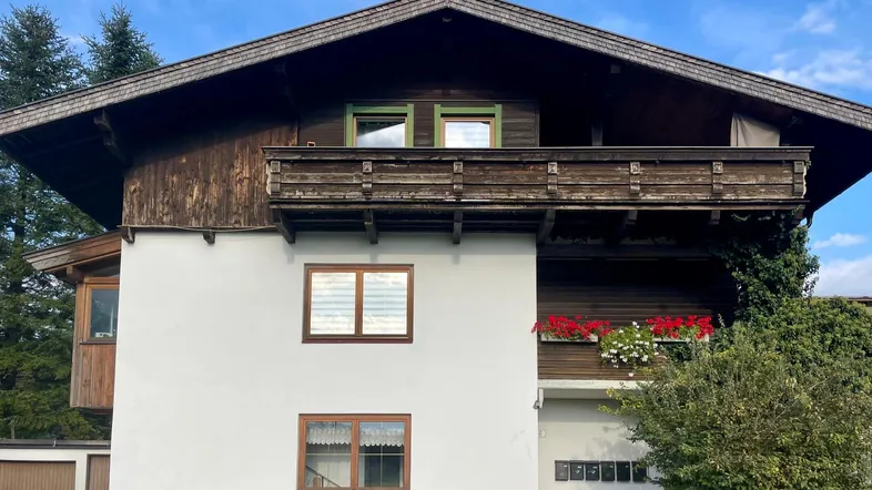 Traditionelles Haus mit weißer Fassade, Holzverkleidung, Balkon und Satteldach im alpinen Stil.