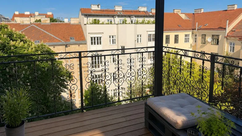 Heller Balkon mit Holzboden, schmiedeeisernem Geländer und Blick auf die umliegenden Gebäude.