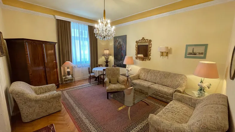 Geräumiges Wohnzimmer mit klassischer Einrichtung, Kronleuchter, Parkettboden und einem Teppich.
