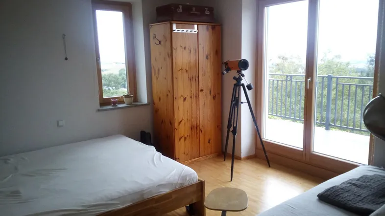 Helles Schlafzimmer mit zwei Betten, Holzschrank und Zugang zu einem Balkon mit Weitblick.