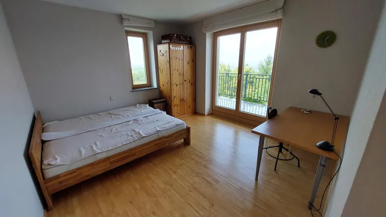 Helles Schlafzimmer mit Holzboden, Zugang zum Balkon und weitem Blick ins Grüne.
